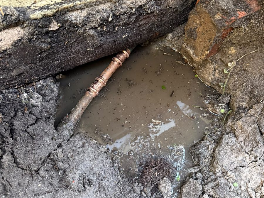 Excavated water leak repair exposing a damaged copper pipe
